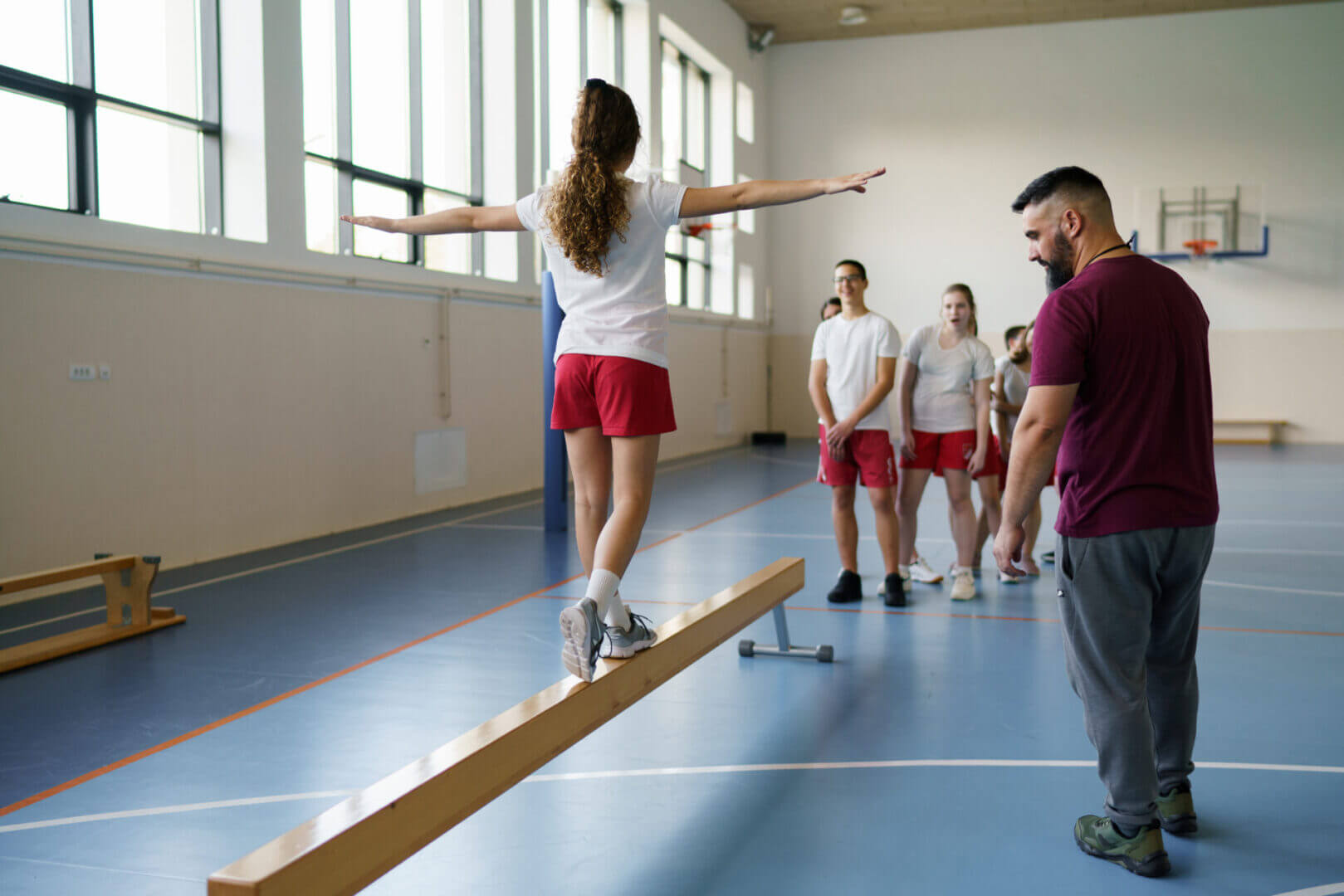 A young girl balancing on a beam with a coach watching.