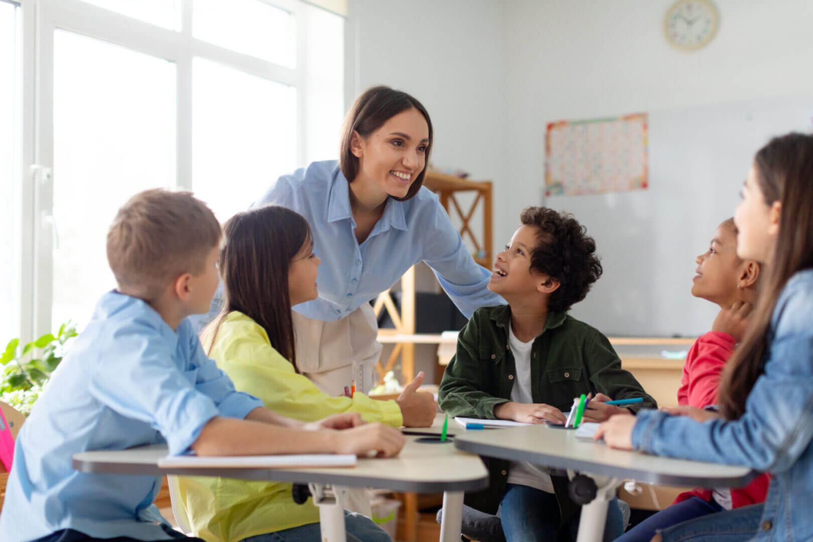 Teacher engaging with diverse students in a bright classroom.